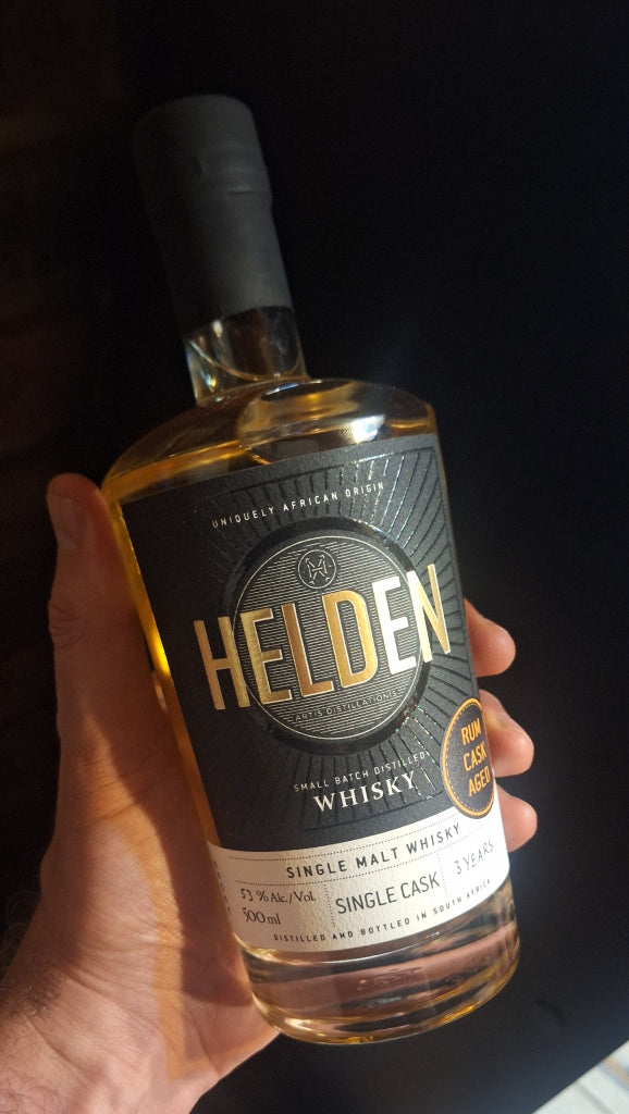 Bottle of Helden Whisky held in a hand against a dark background