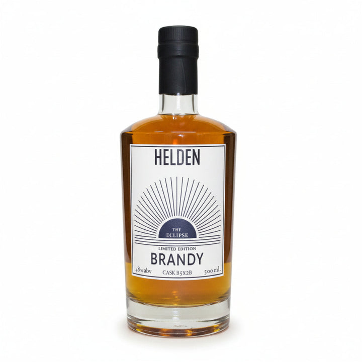A bottle of Helden The Eclipse Limited Edition Brandy, showing the amber liquid inside a clear glass bottle with a white label and a black cap, set against a plain white background.